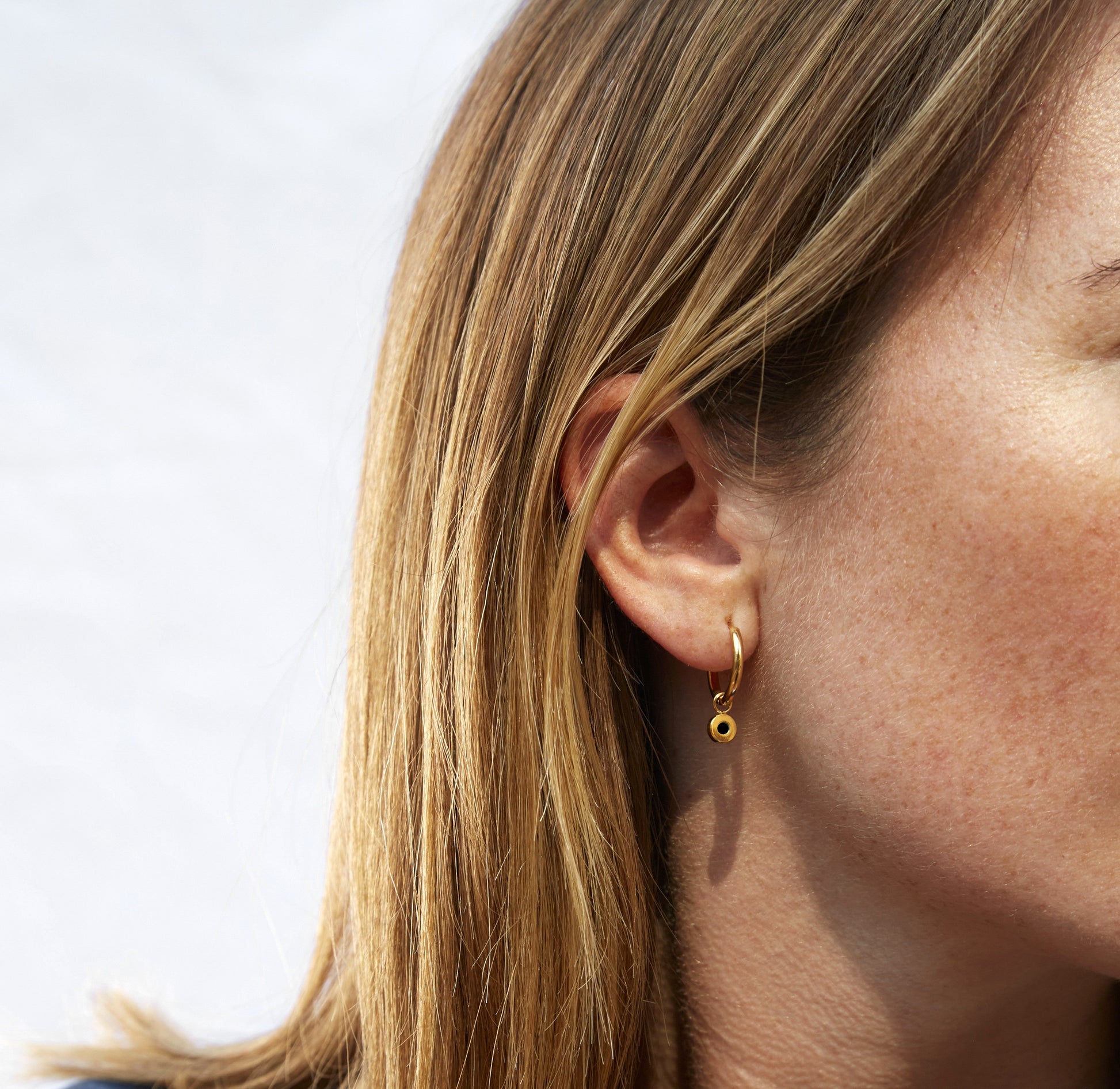 Gold hoop earring with black charm worn on a woman’s ear 
