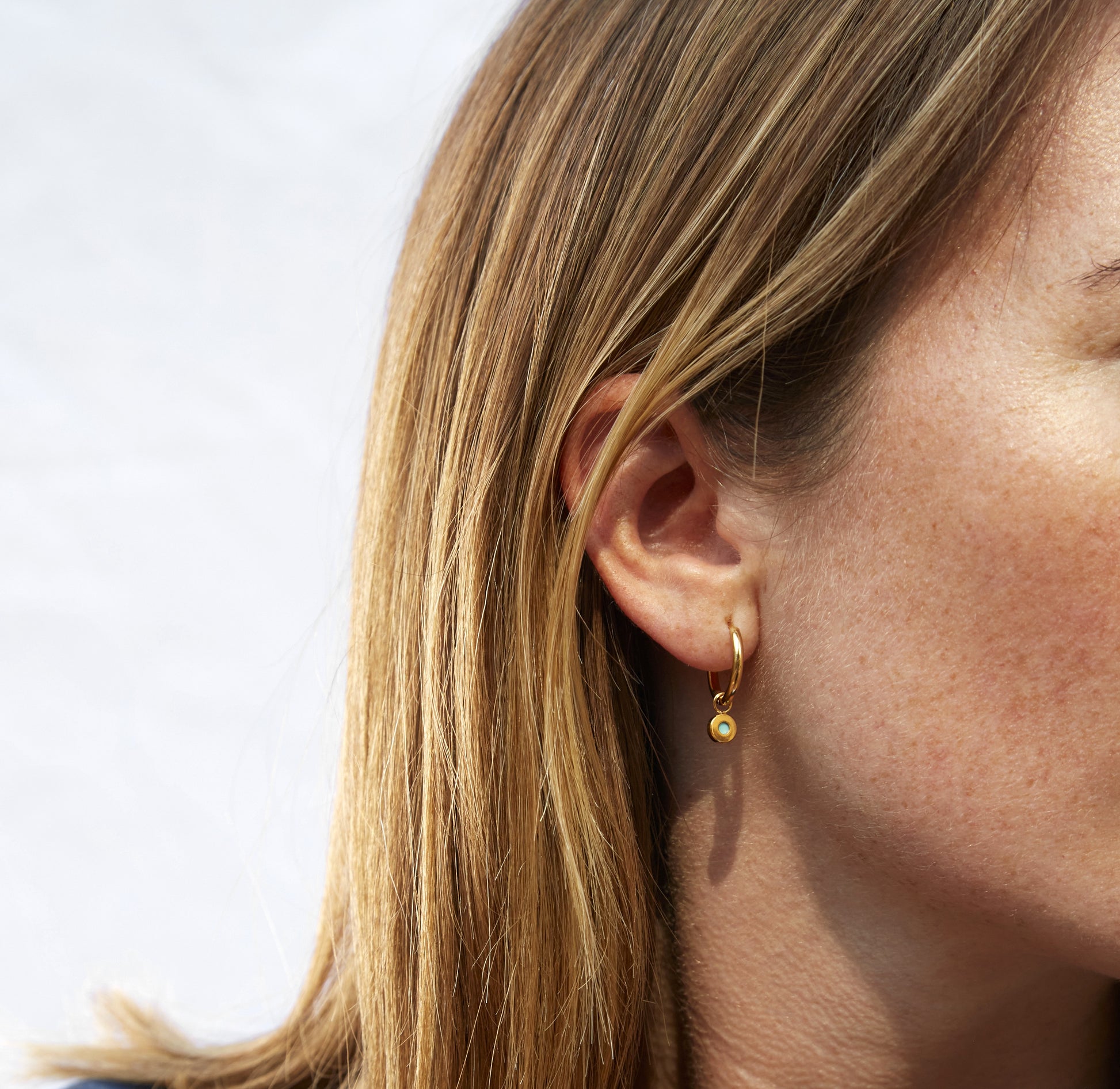 Gold hoop earring with white recycled ocean plastic charm worn on ear 
