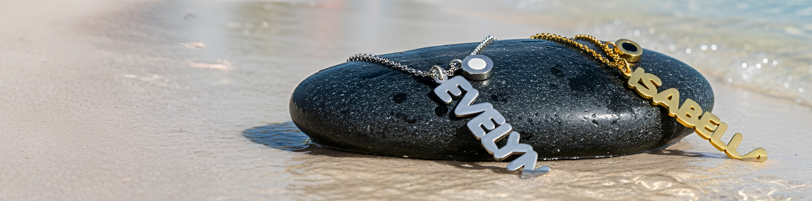 Two Aquaname Beach Banners one silver EVELYN and one gold ISABELL resting on a wet black stone