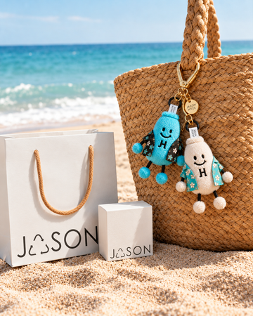 A wicker beach bag with two character keychains, next to a branded paper bag and box.