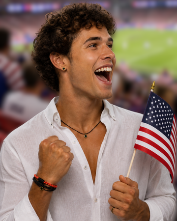 A happy young man with curly hair cheers in a stadium holding a US flag, wearing two stackable Jason Hyde bracelets