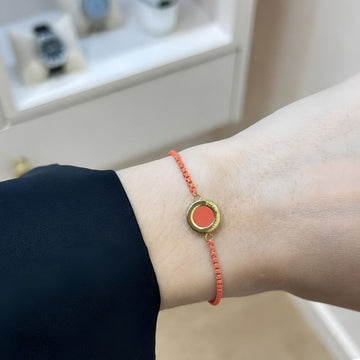 Close-up of a minimalist gold and coral-colored cord bracelet by Jason Hyde worn on a wrist.