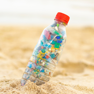 Plastic bottle filled with colorful plastic pieces on beach sand.