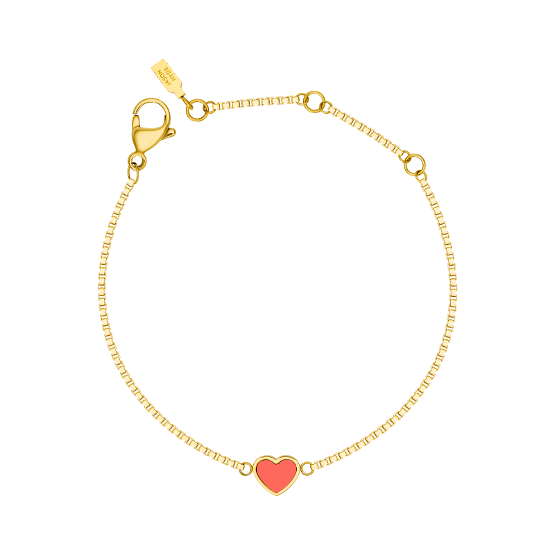 A delicate gold-tone chain bracelet by Jason Hyde featuring a single, small coral-colored enamel heart charm