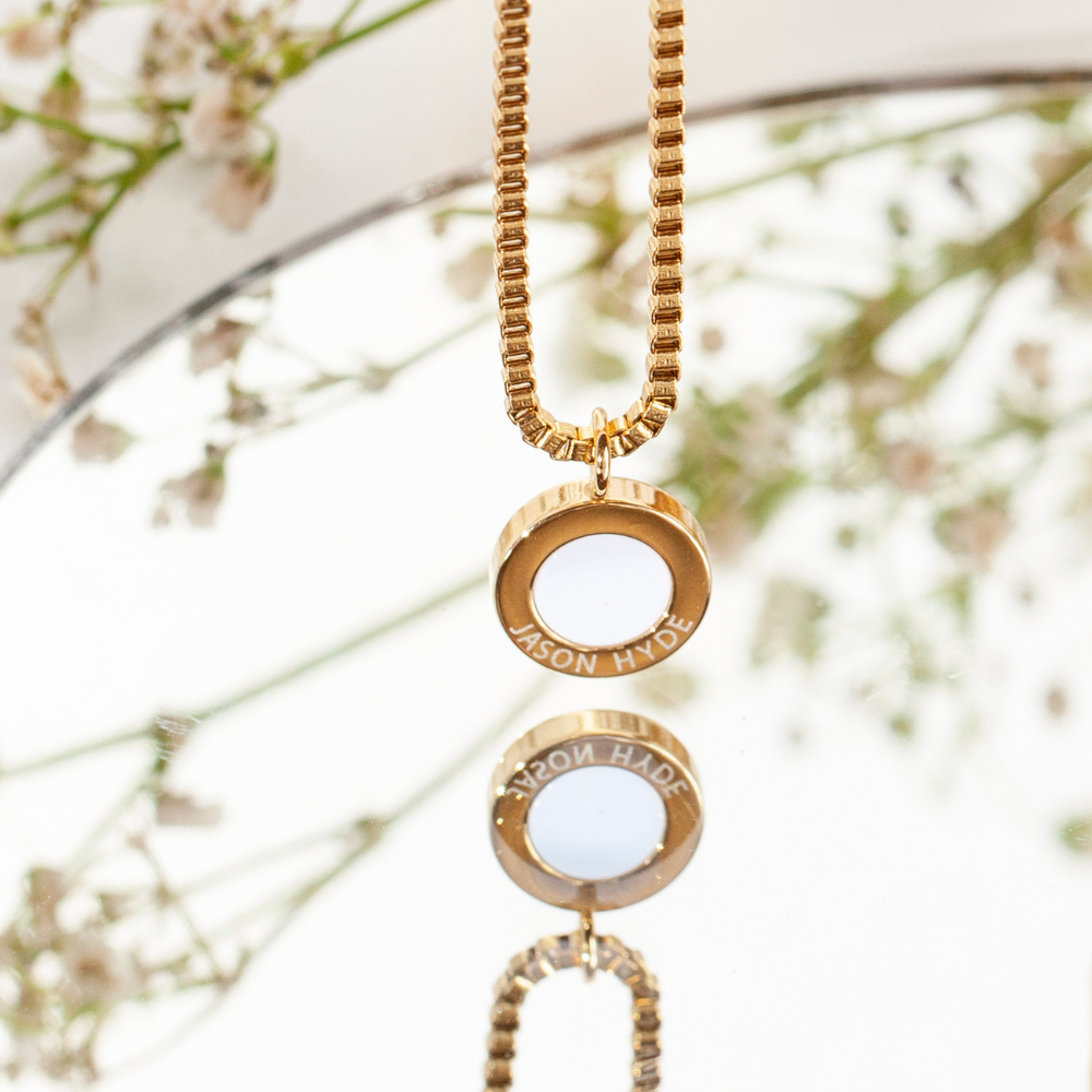 Gold necklace with "JASON HYDE" pendant, reflected.