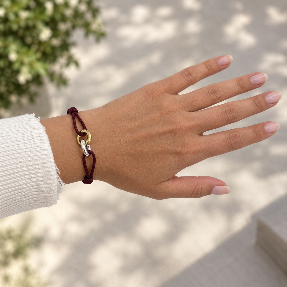 Woman wearing a Jason Hyde burgundy cord bracelet with interlocking gold and silver rings