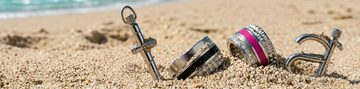 Silver pendants partially buried in beach sand with ocean background.