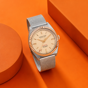 Jason Hyde stainless steel mesh watch with gold-tone dial on orange background.