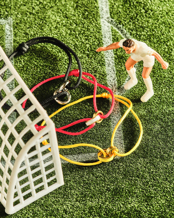 Miniature soccer player figure near three Jason Hyde cord bracelets on a green turf field.