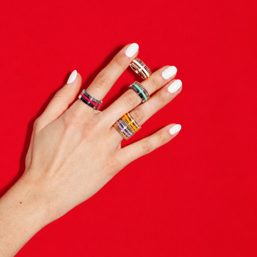 Jason Hyde colorful enamel and gold stacking rings worn on a hand with white manicure against a bright red background.