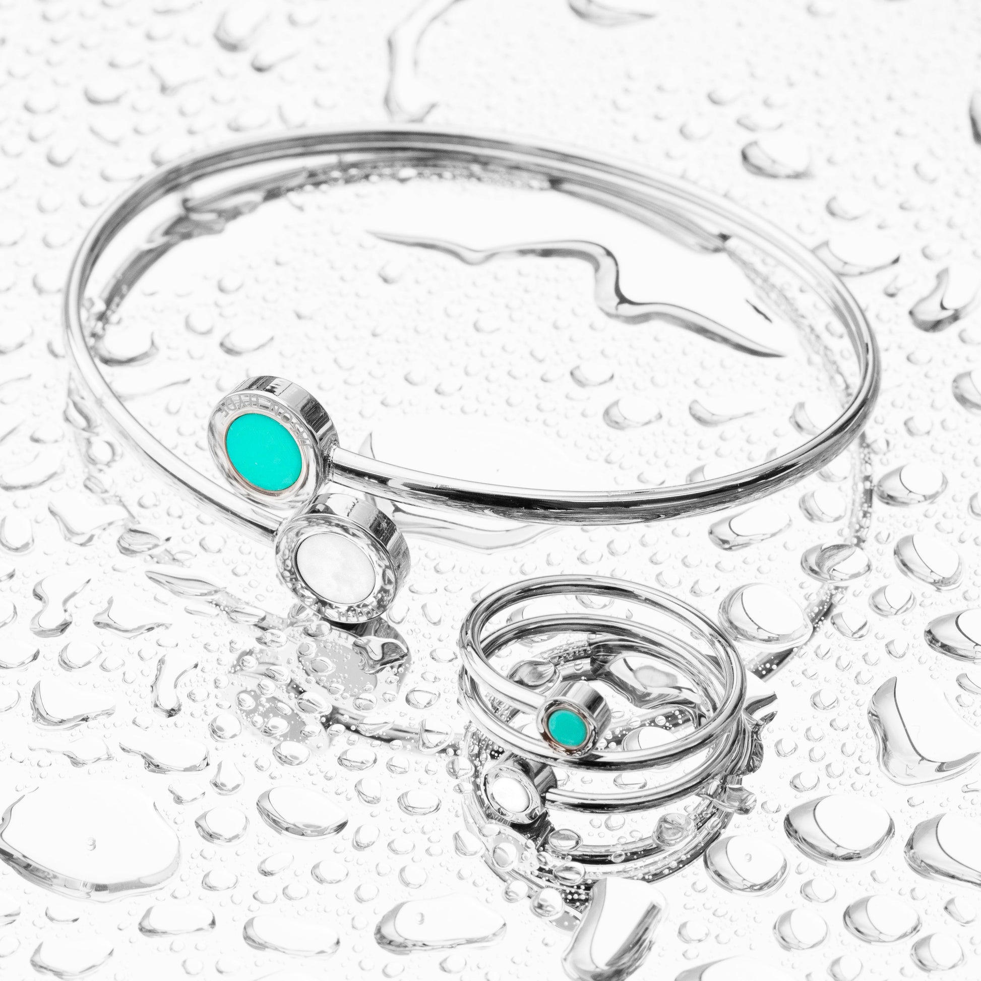 Silver bangle bracelet and a ring with  on a water droplet surface.
