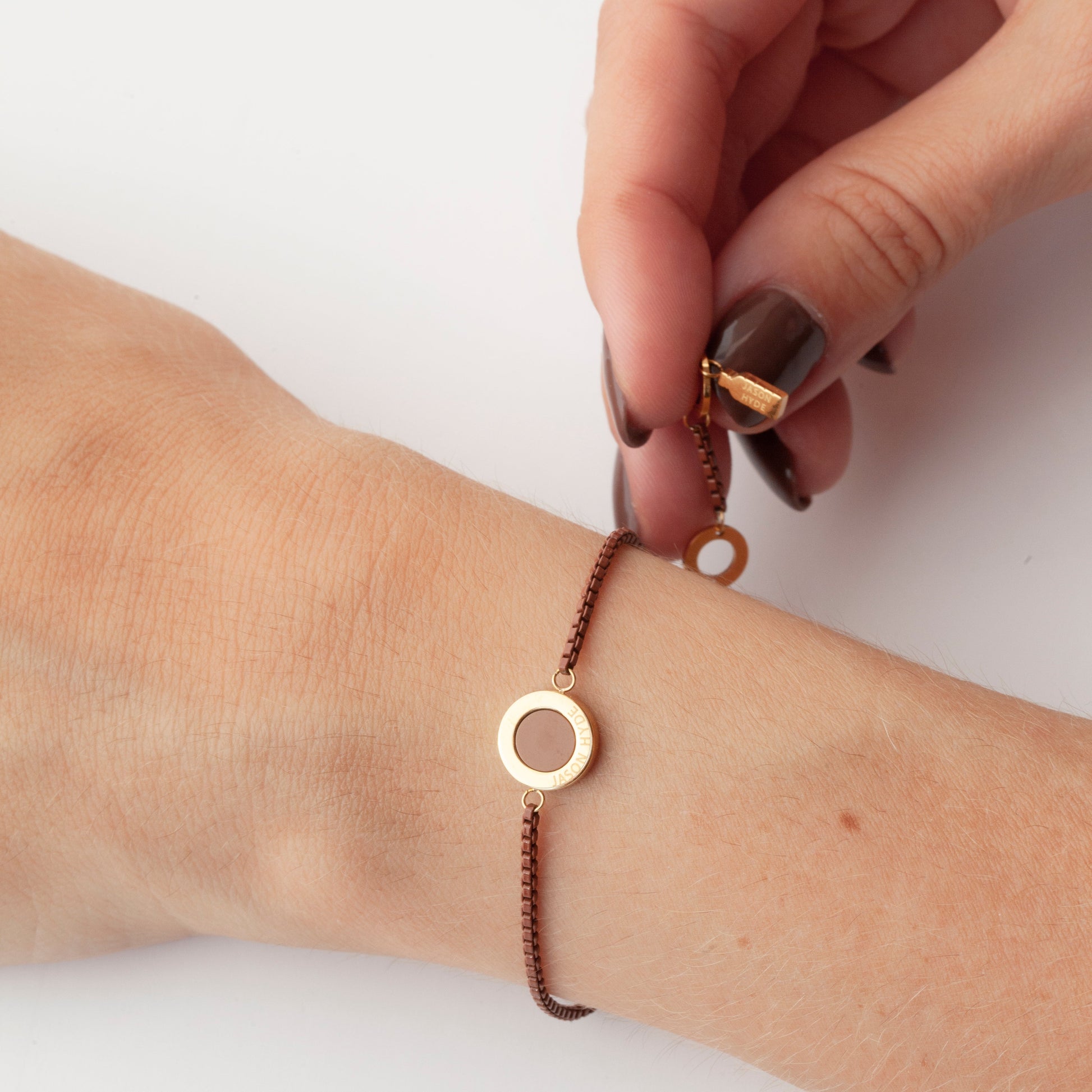 Woman's hand holding a gold bracelet with a nutshell pendant over the wrist.