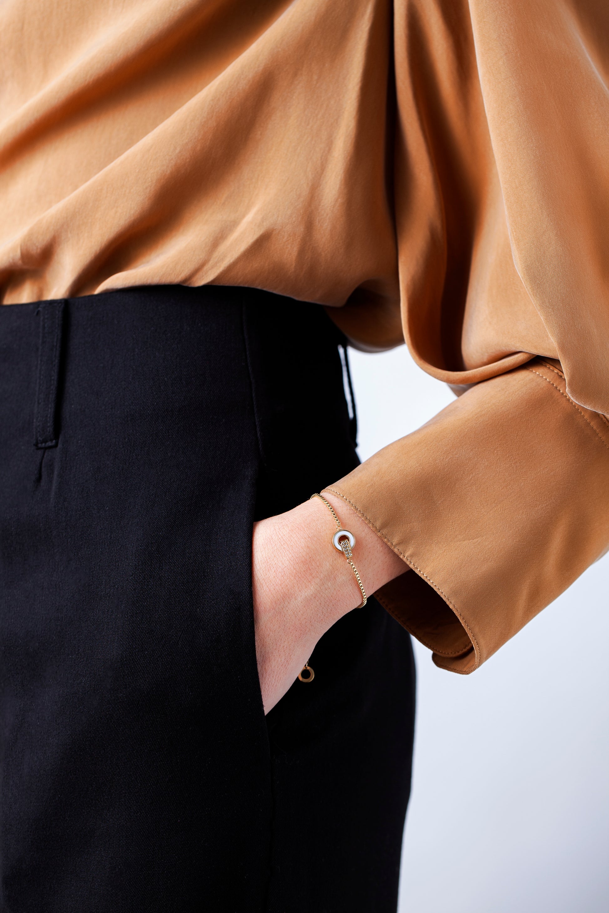 Gold bracelet with zirconia and a white charm on a woman's wrist.