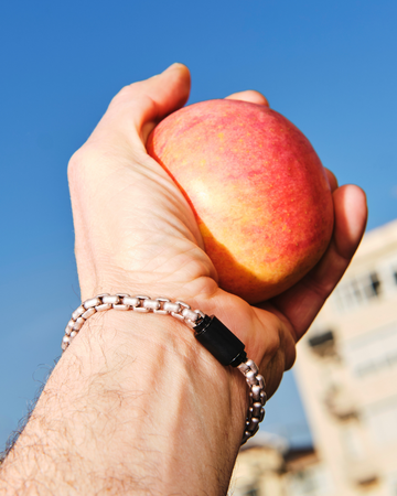 A man's hand holding a red apple against a blue sky, wearing a Jason Hyde silver thick box chain bracelet