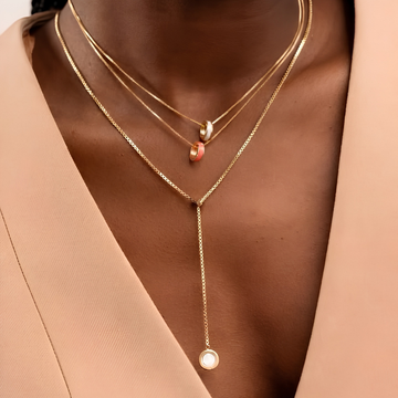 Close-up of minimalist layered gold chains with coral and white accents.