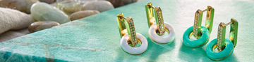 Jason Hyde luxury huggie earrings in gold with white and turquoise recycled plastic charms on a teal stone surface.