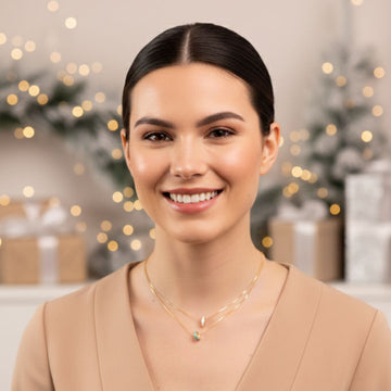 Smiling woman wearing delicate layered gold necklaces against a blurred Christmas background.
