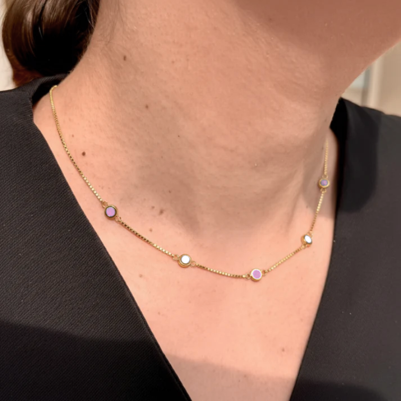 Woman wearing Jason Hyde gold five-charm necklace with colorful minimalist details and elegant styling.