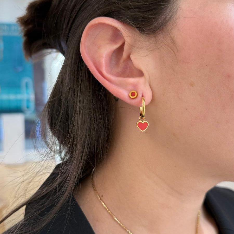 Gold hoop earring with a red heart pendant and a small gold stud worn on an ear
