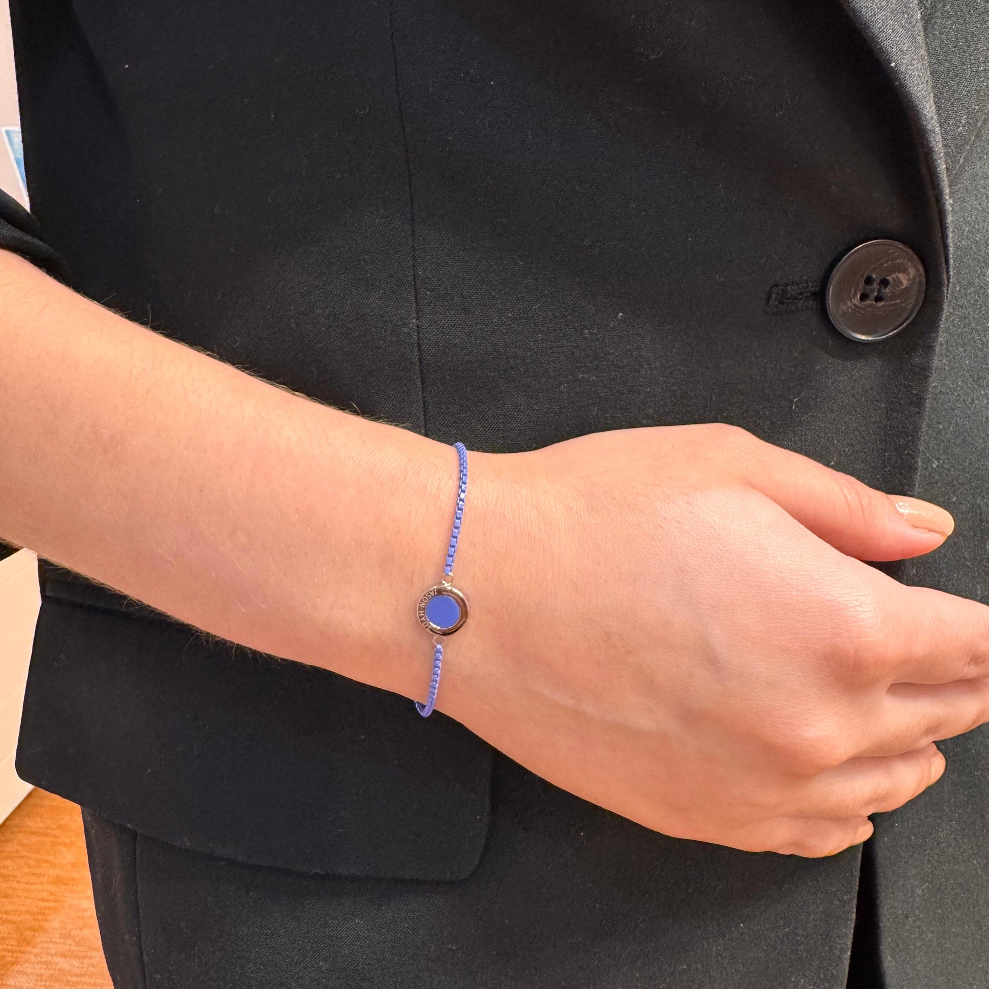 Blue cord bracelet with gold and blue pendant on a wrist.