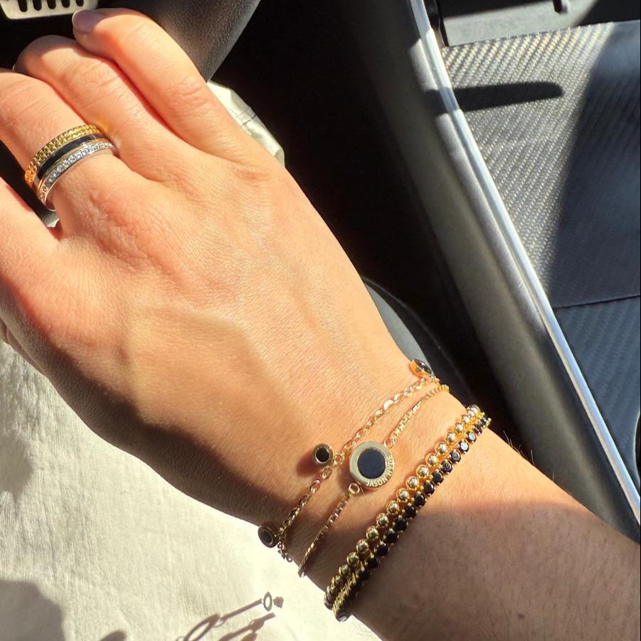 Hand with layered gold bracelets with black details and stacked rings.