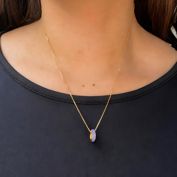 Woman wearing a gold necklace with a persian blue ring pendant.