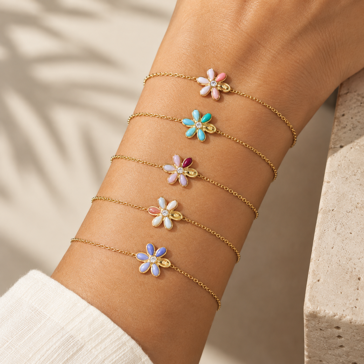 Stacked gold chain bracelets featuring flower charms on a model's wrist.