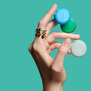 Hand with a gold ring, holding three colorful recycled plastic bottle caps.