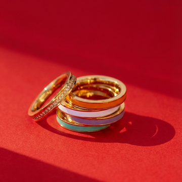 A stack of colorful enamel and gold rings on a red surface