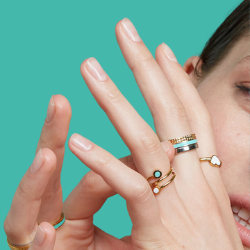 A close-up of a woman's hands, smiling, and showcasing a variety of Jason Hyde gold rings
