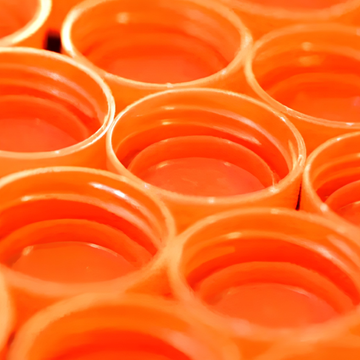 Close-up of numerous recycled bright orange plastic bottle caps.