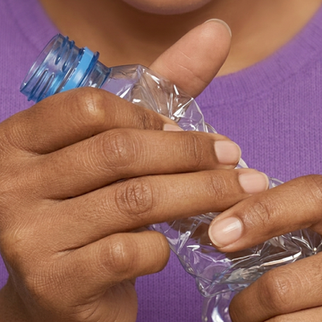 Hands crushing a clear plastic water bottle to be upcycled