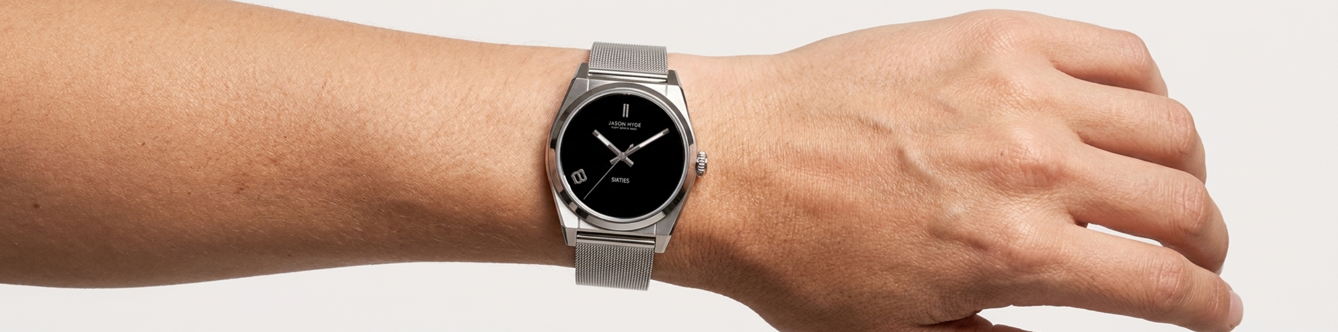 A person wearing a silver Jason Hyde watch with a black dial and mesh strap.