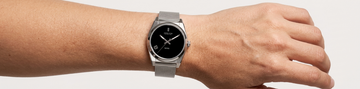 A person wearing a silver Jason Hyde watch with a black dial and mesh strap.