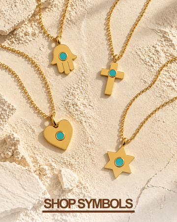 Four gold-tone symbol necklaces laid out on a textured beige surface: a hamsa hand, a cross, a heart, and a star, each with a small turquoise plastic chip center. The text 'SHOP SYMBOLS' appears in the bottom.