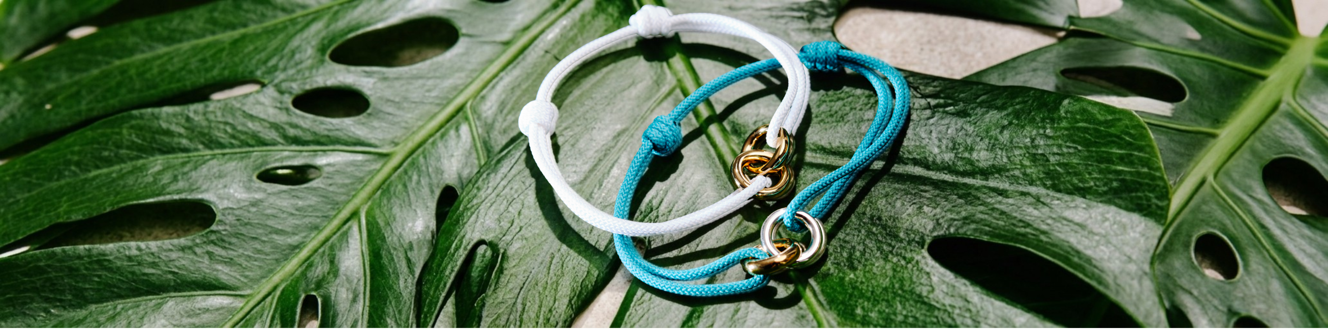 Close-up of two Jason Hyde sustainable cord bracelets in white and turquoise