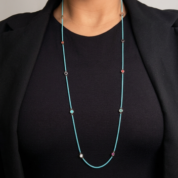 Close-up of a person wearing a sustainable long turquoise cord necklace with colorful recycled charms