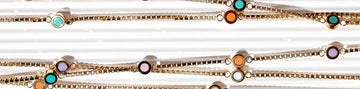 Several gold chains with small, colorful enamel circular pendants on a white textured surface.