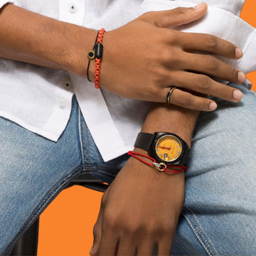 Man wearing an orange bracelet, a black watch with a yellow face, and a gold ring.