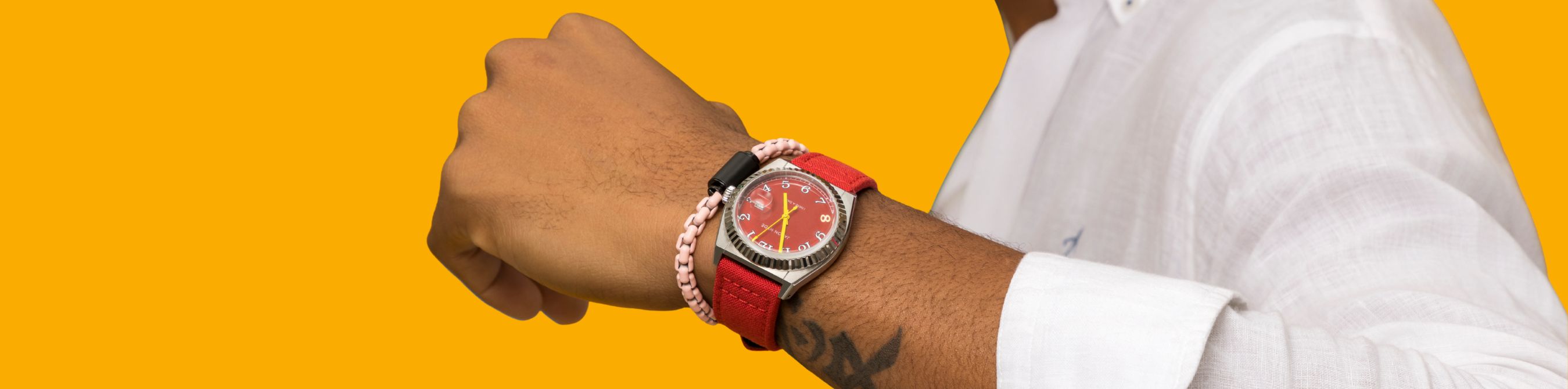 Close-up of a person's arm wearing a red-strapped watch and a light pink chain bracelet