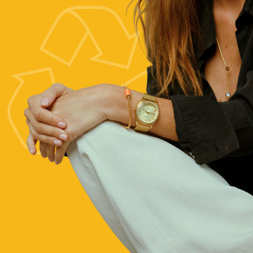 A woman wearing a gold watch and a coral-beaded bracelet on her wrist
