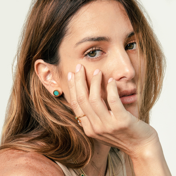 Gold rings and stud earrings with turquoise chips worn by a woman