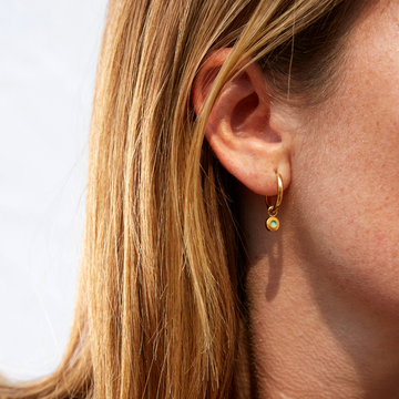 Close-up of a gold hoop earring with a small turquoise charm on a woman's ear.