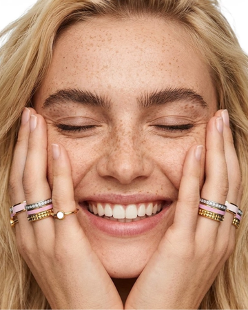 Woman with eyes closed wearing Jason Hyde stacked pink enamel, and gold rings on her fingers.