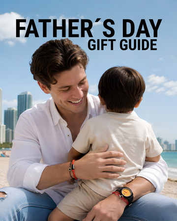 A smiling man in a white shirt and jeans sits on a beach, warmly hugging his young son