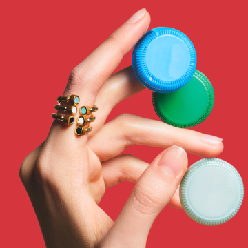 Hand holding three plastic bottle caps while wearing a gold statement ring