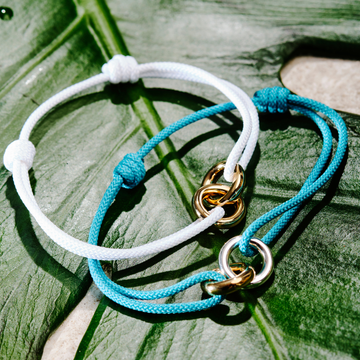 Jason Hyde turquoise and white cord bracelets with gold and silver ring accents on a leaf.