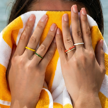 Model wearing stacked colorful enamel and diamond rings on a beach towel.