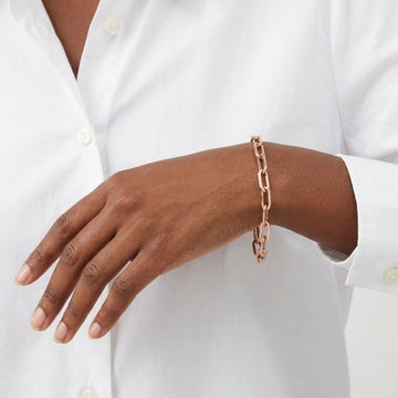 Gold paperclip chain bracelet on a model wearing a white button-down shirt.