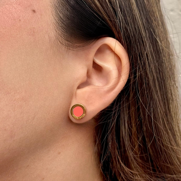 Close-up of a model wearing a gold Jason Hyde stud earring with a circular coral-colored center detail.